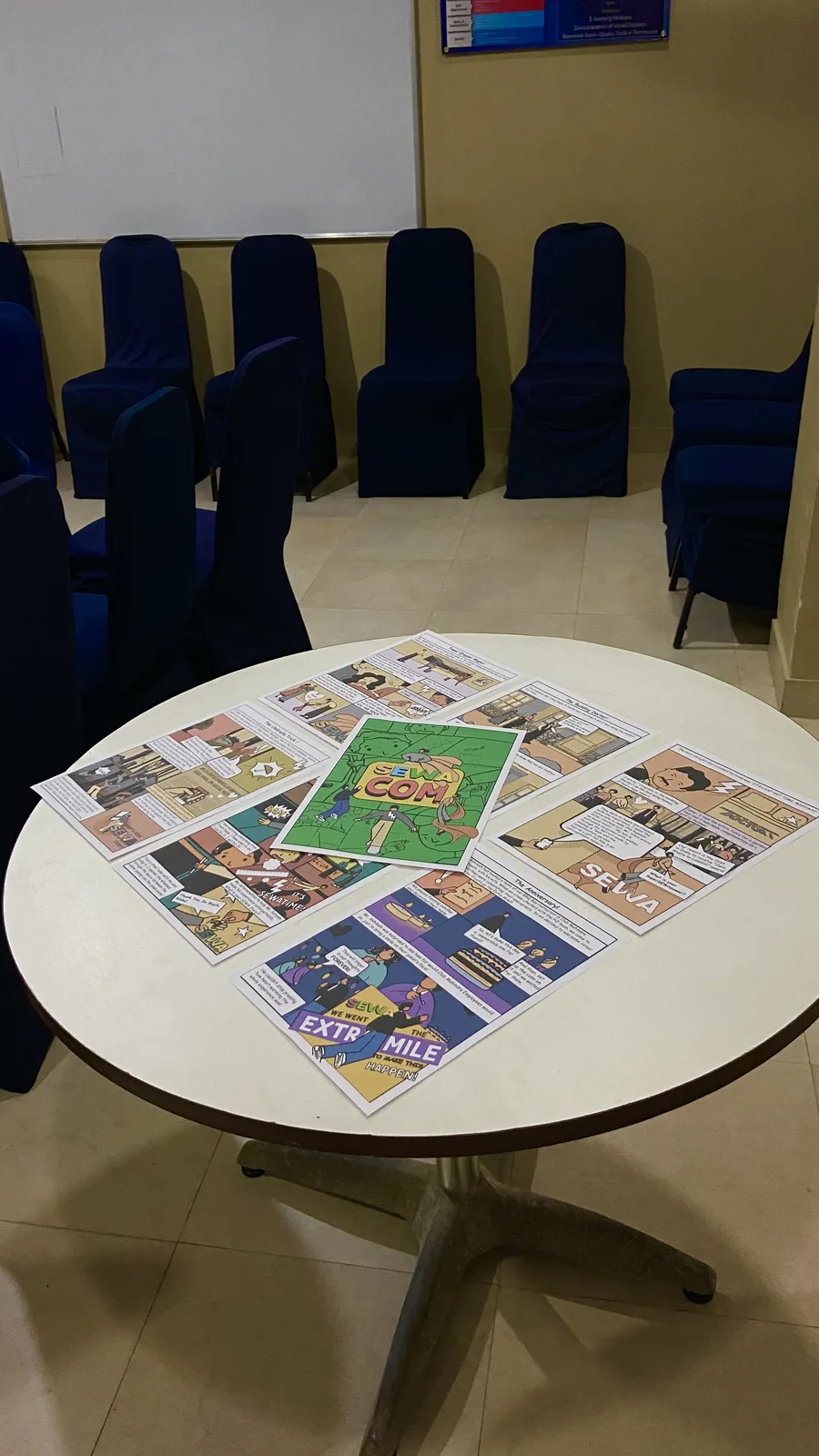 Printed SEWA comic draft pages spread across a round white table in Coorg.