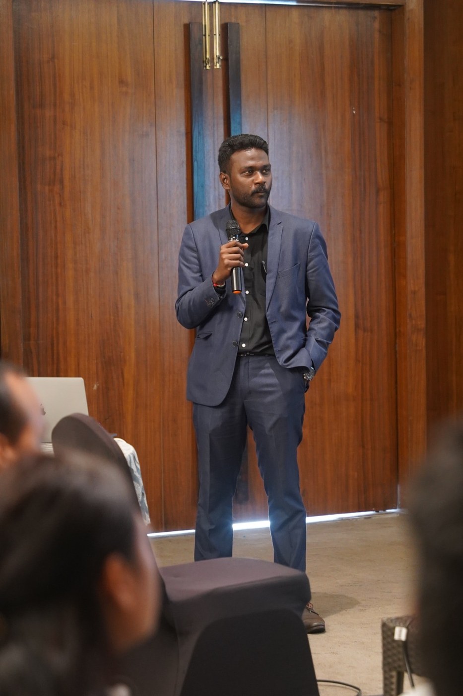 Naveen presenting with a handheld microphone to an audience in a wood-panelled room at Courtyard by Marriott, Mahabaleshwar.