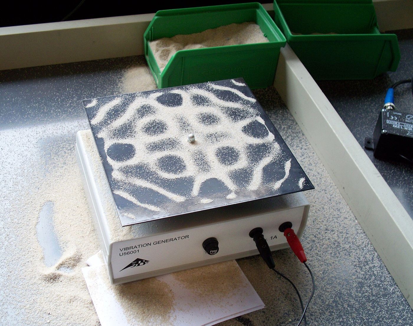 A square metal plate with sand gathered into a symmetrical standing-wave pattern.