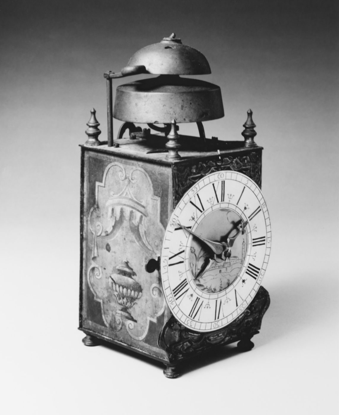 An eighteenth-century table clock movement in a metal case, with a bell on top and an enamel dial.